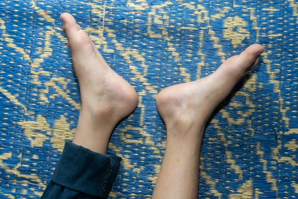 Küçük çocuğun bacakları mavi plastik paspasın üzerinde uzanıyordu. Genç ayaklar