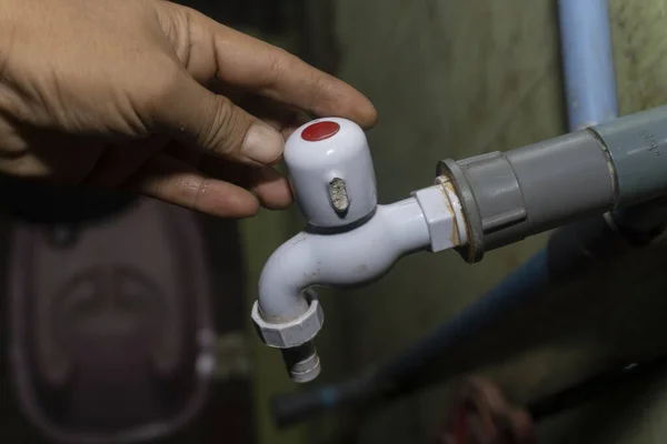 Karanlık bir arka planda beyaz su musluğunu açan biri. Su musluğu ile boru bağlantısı