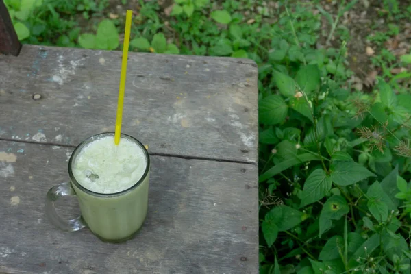 Ahşap bir masada kocaman bir bardak avokado suyu. Temiz cam bardaklarda ve plastik pipetlerde avokado suyu