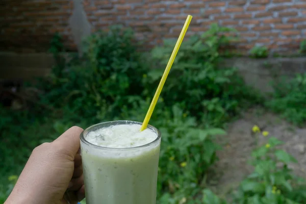 Biri elinde kocaman bir bardak avokado suyu tutuyor. Temiz cam bardaklarda ve plastik pipetlerde avokado suyu