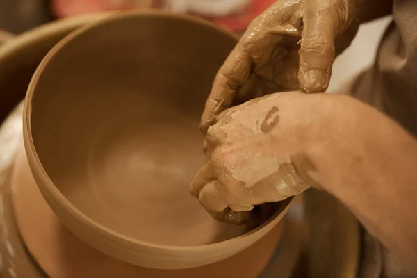 Close-up of a male potter shaping a piece of wet clay into a bowl with his hands on a pottery wheel in a ceramic studio