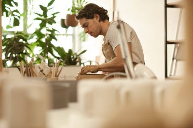 Young male ceramist shaping a piece of clay into a bowl while working at a pottery wheel in a ceramic studio clipart