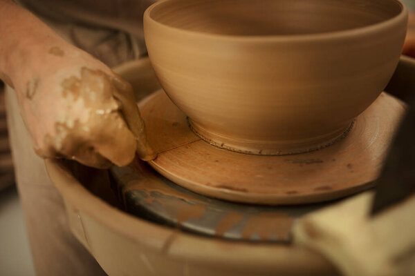 Close-up of a male potter using a wire to remove a freshly sculpted bowl n a pottery wheel in a ceramic studio