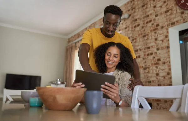 一对年轻的多民族夫妇在厨房一起喝咖啡的时候 一边笑一边看数码平板电脑上的东西 — 图库照片