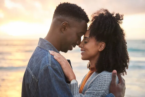 互いの腕の中で目を閉じて 日没時にビーチで笑顔で立っている若い多民族のカップルを愛情 — ストック写真