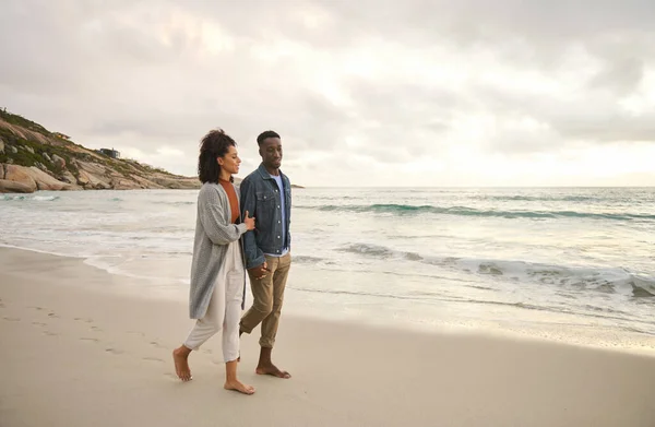 雲の多い午後に砂浜を手に手を取りながら話している若い多民族のカップルの笑顔 — ストック写真