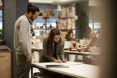 Female ceramics studio manager going over paperwork while working at a table with a team member clipart