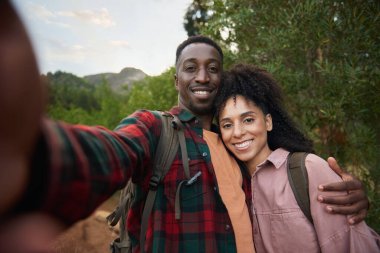 Yazın engebeli tepelerde yürüyüş yaparken gülümseyen ve selfie çeken genç çiftlerin portresi.