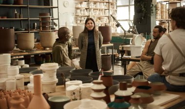 Smiling young female ceramics studio owner talking with her diverse team of potters and ceramists during a meeting clipart