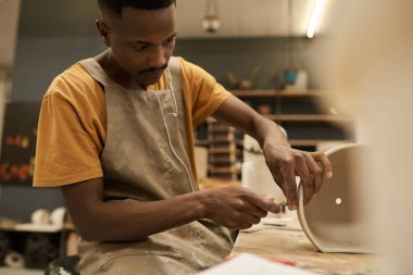 Genç Afrikalı bir seramist çömlek imalat atölyesindeki bir tezgahta delik açmak için matkap ucu kullanıyor.