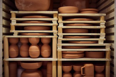 Assortment of plates and bowls in stacks on shelves inside of a kiln an ceramist workshop clipart