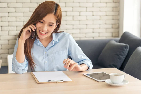 Asian women talk via smartphone work from home small office desk. Young asian Woman hands holding phone technology lifestyle. Happy Women person calling use digital smart phone working home office