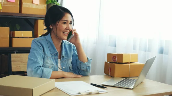 Online seller entrepreneur young asian woman using phone calling, checking online order. Woman calling check goods stock, delivery package shipping. Asian woman startup small business at home office