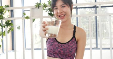 Kadın elleri şişeden akan beyaz süt bardağını tutuyor. Asyalı kadınlar güler, kameralı sağlık hizmetleri yaşam tarzına bakarlar. Güzel bayan az yağlı süt içen laktozsuz süt.