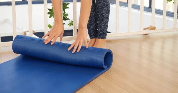 Woman hands rolled up yoga mat on gym floor in yoga fitness training room. Home workout woman close up hands rolling foam yoga gym mat. Woman barefoot home workout sportive healthy lifestyle concept
