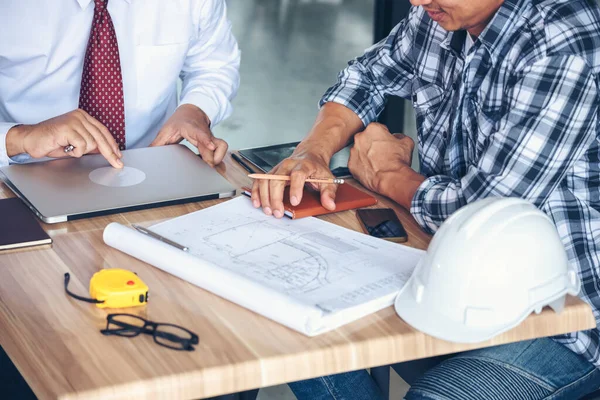 Contractor construction engineer meeting talking together on architect table at construction office site. Businessman engineer manager discuss with foreman team builder look at plan blueprint laptop