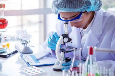 Asian Woman scientist hand write note research in medical lab look at science microscope medical test. Researcher biology chemistry. Asian Female technician laboratory using microscope blood test