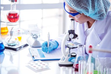 Tıp laboratuarındaki kadın bilim adamı el yazısı bilgileri mikroskop tıbbi testleri, biyoloji kimyasını inceler. Asya kadın teknisyen laboratuarı kan testi farmasötik analizi yapıyor.