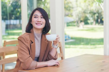 Kahve dükkanında elinde taze fincanla sade kahve içen güzel kadın. Kahve sever. Asyalı kadın, yeşil bahçe kafesinde elinde fincanla sade kahve içiyor. Genç kadın gülümse aşkım, kahve iç.