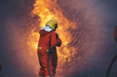 Firefighter Rescue training in fire fighting extinguisher. Firefighter fighting with flame using fire hose chemical water foam spray engine. Fireman wear hard hat, safety suit uniform for protection