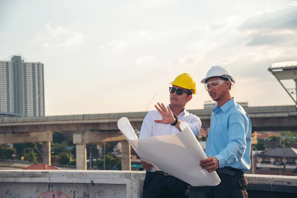 Civil engineer teams meeting working together wear worker helmets hardhat on construction site in modern city. Foreman industry project manager engineer teamwork. Asian industry professional team