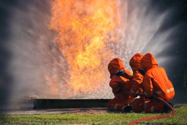 Firefighter Rescue training in fire fighting extinguisher. Firefighter fighting with flame using fire hose chemical water foam spray engine. Fireman wear hard hat, safety suit uniform for protection