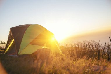 Tent Camping trip outdoor hiking mountain hill. Tent camp in nature background with sunrise on top of mountain. Picnic tent green nature campground in forest. Adventure Travel wildness flare sunlight