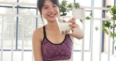 Kadın elleri şişeden akan beyaz süt bardağını tutuyor. Asyalı kadınlar güler, kameralı sağlık hizmetleri yaşam tarzına bakarlar. Güzel bayan az yağlı süt içen laktozsuz süt.