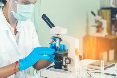 Indian Scientist man look into Microscope research in science laboratory. Asian biochemistry scientist using microscope in laboratory chemistry labs. Covid-19 medical research scientific experiment