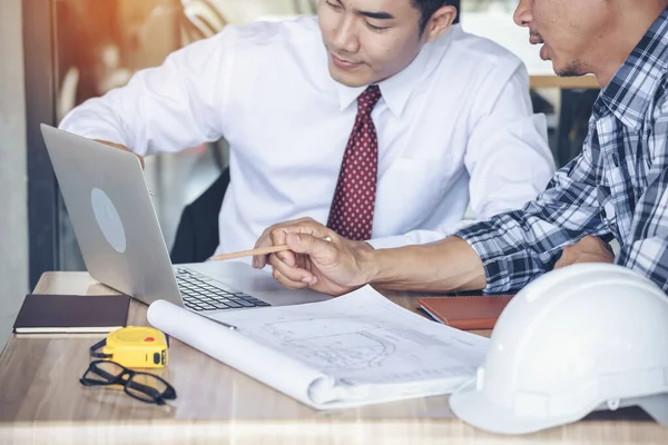 Contractor construction engineer meeting talking together on architect table at construction office site. Businessman engineer manager discuss with foreman team builder look at plan blueprint laptop