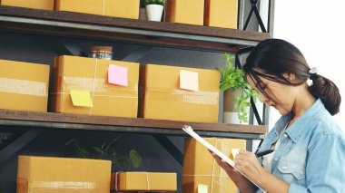 Asyalı bir kadın ev ofisinde küçük bir iş kuruyor. Çevrimiçi satıcı girişimci genç Asyalı kadın çevrimiçi tablet kontrolü kullanıyor. Tablet kullanan kadın stok malları teslimat paketini kontrol et