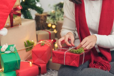 Kadın eli hediyesini sıcak oturma odasına sarın. Noel ağacının altında hediye paketi yapan bir kadın. Asyalı kadın dekoratif balo balosu Noel ağacı Noel 'de kış mevsimi kutlamalarında