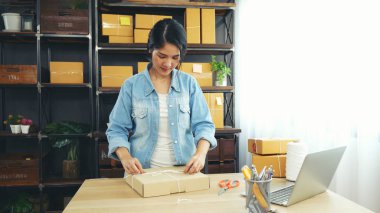 Kadın paket kutusunu masaya koydu. Müşteriye mal teslimatını kontrol ediyor. Asyalı bir kadın ofis masasında küçük bir iş kuruyor. Girişimci Asyalı kadın teslimat için ürün topluyor