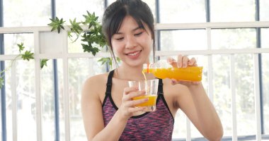 Kadın elleri soğuk portakal suyu tutuyor taze meyve suyu içiyor. Asyalı kadınlar güler, kameralı sağlık hizmetleri yaşam tarzına bakarlar. Güzel bir kadın kokteyl şişesinden portakal suyu dolduruyor.