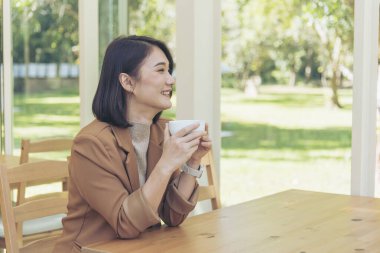 Kahve dükkanında elinde taze fincanla sade kahve içen güzel kadın. Kahve sever. Asyalı kadın, yeşil bahçe kafesinde elinde fincanla sade kahve içiyor. Genç kadın gülümse aşkım, kahve iç.