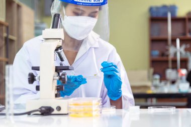 Tıp laboratuarındaki kadın bilim adamı el yazısı bilgileri mikroskop tıbbi testleri, biyoloji kimyasını inceler. Asya kadın teknisyen laboratuarı kan testi farmasötik analizi yapıyor.