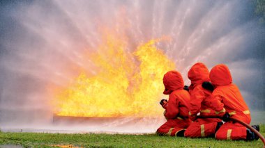 Firefighter Rescue team training in fire fighting extinguisher. Firefighter teamwork fighting with flame using fire hose chemical water foam spray engine. Fireman wear hard hat, safety suit uniform