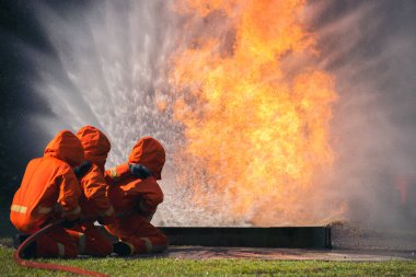 Firefighter Rescue training in fire fighting extinguisher. Firefighter fighting with flame using fire hose chemical water foam spray engine. Fireman wear hard hat, safety suit uniform for protection
