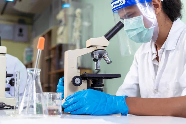Indian Scientist man look into Microscope research in science laboratory. Asian biochemistry scientist using microscope in laboratory chemistry labs. Covid-19 medical research scientific experiment