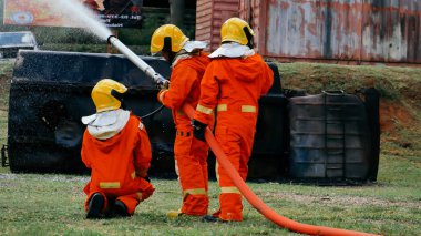 Firefighter Rescue team training in fire fighting extinguisher. Firefighter teamwork fighting with flame using fire hose chemical water foam spray engine. Fireman wear hard hat, safety suit uniform