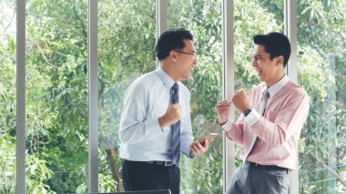 Excited two businessman ceo company achievement. Success Businessman happy got good news mobile smartphone. Asian young businessman raises hand happy, smiling, excited got great news from phone lucky