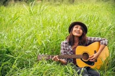 Yeşil parkta akustik gitar çalan genç kadınlar. Evde akustik gitar enstrümanı çalan bir kadın, güzel doğada genç Asyalı müzisyen kız yaşam tarzı. Mutlu gitarist
