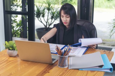 Ev ofis masasında dizüstü bilgisayar kullanan Asyalı kadın serbest yazar. Finansal grafik çizelgesi okuyan kadın pazarlama verilerini analiz ediyor. Ofiste çalışan Asyalı kadınlar, iş konuları, kahve fincanları.