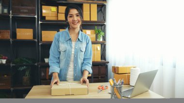 Kadın paket kutusunu masaya koydu. Müşteriye mal teslimatını kontrol ediyor. Asyalı bir kadın ofis masasında küçük bir iş kuruyor. Girişimci Asyalı kadın teslimat için ürün topluyor