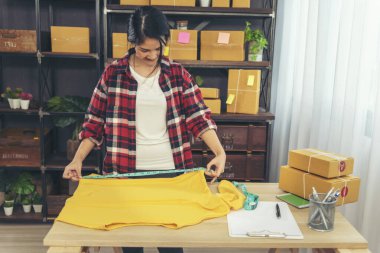 Moda tasarımcısı kadınlar masadaki giysi tasarımı kutusunu ölçüyorlar. Kadınlar mal boyutlarını kontrol ediyor, teslimat paketinin kalitesini ölçüyorlar. Girişimci Asyalı kadın ofis masasında küçük bir iş kurdu