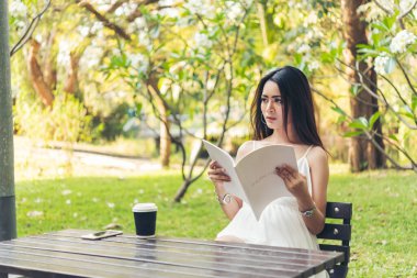 Green Park 'ta elinde kitap okuyan Asyalı bir kadın. Genç kadın rahatlama açık kitap kişisel çalışma okudu. Üniversiteli kadınlar mutluluktan gülümsüyor. Kadınlar yeşil parkta oturuyor.