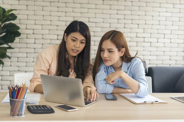 Two asian Female freelance reading financial graph charts Planning analyzing marketing data. Asian people team working office firm. Two businesswomen team meeting using laptop at company office desk.