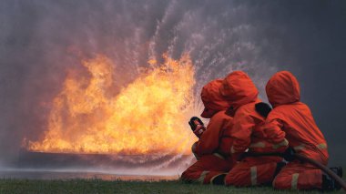 Firefighter Rescue team training in fire fighting extinguisher. Firefighter teamwork fighting with flame using fire hose chemical water foam spray engine. Fireman wear hard hat, safety suit uniform