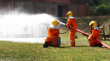 Firefighter Rescue team training in fire fighting extinguisher. Firefighter teamwork fighting with flame using fire hose chemical water foam spray engine. Fireman wear hard hat, safety suit uniform
