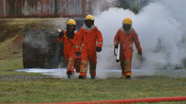 Firefighter Rescue team training in fire fighting extinguisher. Firefighter teamwork fighting with flame using fire hose chemical water foam spray engine. Fireman wear hard hat, safety suit uniform